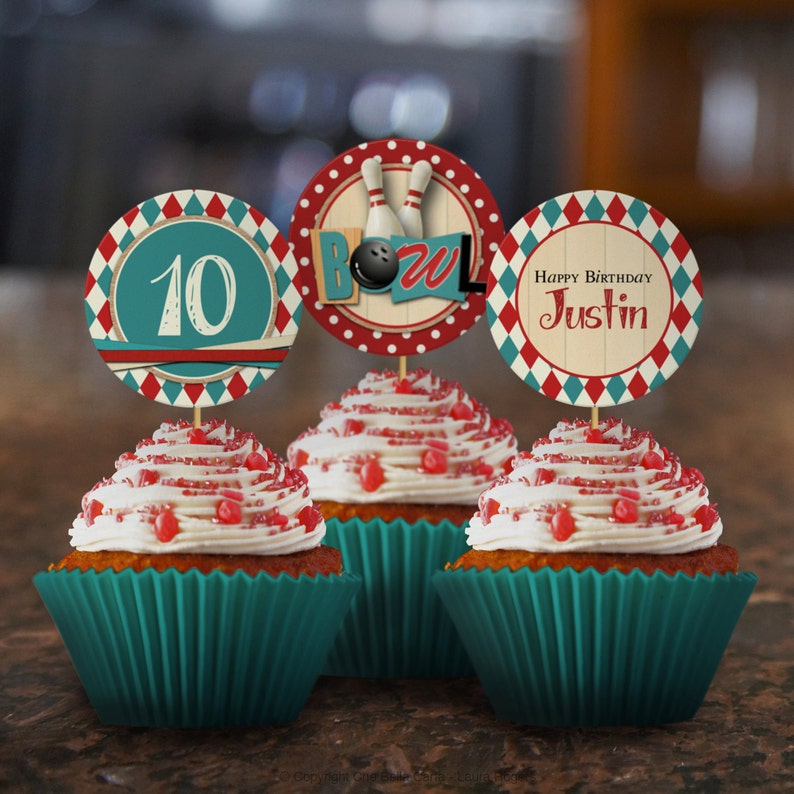 May include: Three teal cupcake liners with white frosting and red sprinkles. Each cupcake has a round paper topper with a bowling theme. One topper says "Happy Birthday Justin", another says "10", and the third has a bowling ball and pins with the word "Bowl".