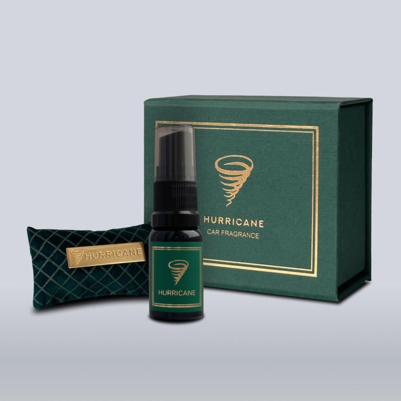 May include: A car fragrance set featuring a dark green bottle with a black spray top, a small green velvet pouch, and a dark green box. The bottle and box have gold accents and the word "HURRICANE" is printed on them.