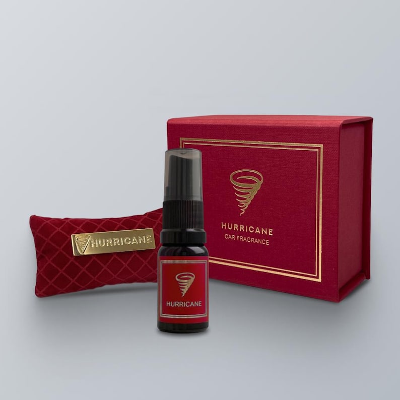 May include: A car fragrance set featuring a red box and a matching red velvet pouch. The set includes a small black spray bottle with a red label and the word "Hurricane". The box and pouch have gold accents and the Hurricane logo.