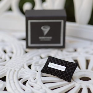 May include: A black box with a white border and a stylized tornado logo. A small black pillow with a diamond pattern and a white label that reads "HURRICANE" is in front of the box.