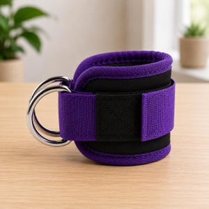 Puede incluir: Una correa de tobillo morada y negra con un anillo en D para entrenamientos en el gimnasio. La correa tiene un cierre de velcro para un ajuste seguro. Fabricada con materiales duraderos y diseñada para ejercicios de resistencia.