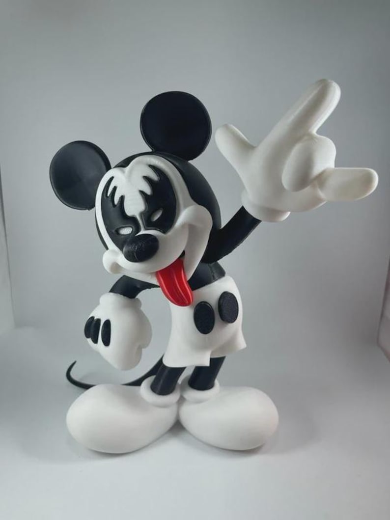 May include: A black, white, and red figurine of Mickey Mouse in a rock and roll pose. The figurine has a black and white face design, a red tongue, and white gloves. The figure is wearing white shorts and large white shoes.