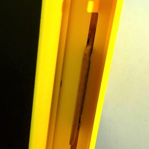 Peut inclure: Un cadre rectangulaire en plastique jaune vif imprim&eacute; en 3D avec un centre creux. &Agrave; l'int&eacute;rieur du cadre, un insert rectangulaire fin et vertical de couleur beige est positionn&eacute;, maintenu par de petites languettes en plastique jaune.