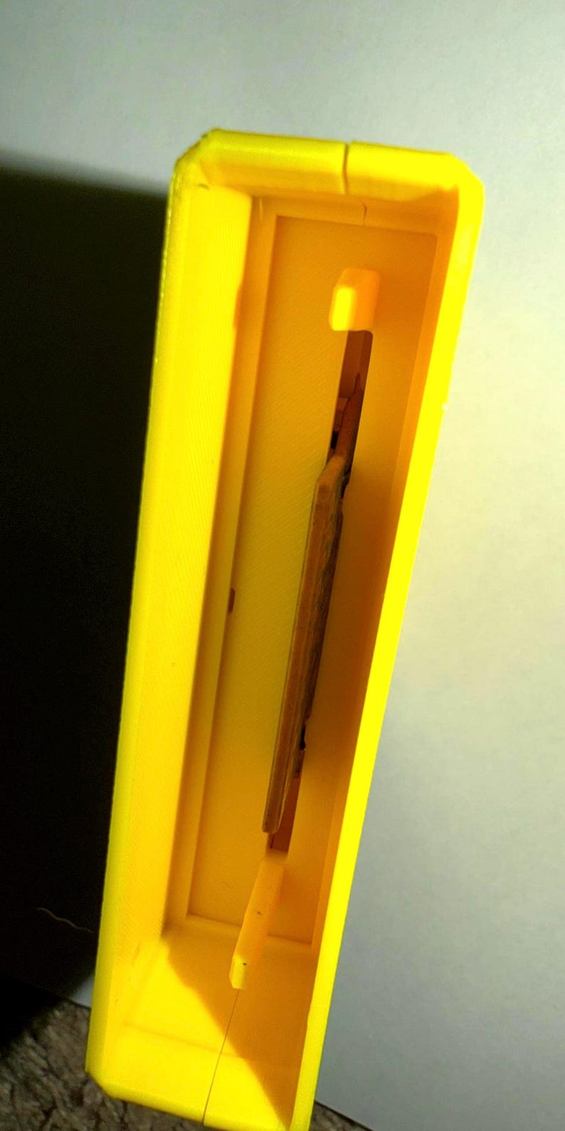 Peut inclure: Un cadre rectangulaire en plastique jaune vif imprim&eacute; en 3D avec un centre creux. &Agrave; l'int&eacute;rieur du cadre, un insert rectangulaire fin et vertical de couleur beige est positionn&eacute;, maintenu par de petites languettes en plastique jaune.