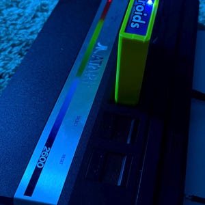 Peut inclure: Une console de jeux vid&eacute;o Atari 2600 noire avec un panneau de commande argent&eacute; portant le logo Atari, les mentions Select et Reset. Une cartouche de jeu Asteroids vert citron vif est ins&eacute;r&eacute;e dans la fente sup&eacute;rieure.