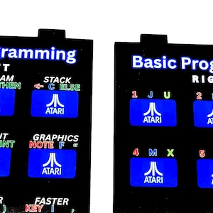 May include: Two black rectangular overlays for an Atari Basic Programming controller. Each features white text reading Basic Programming, with blue buttons labeled with Atari logos and various programming commands, letters, and numbers in white, green, and red.