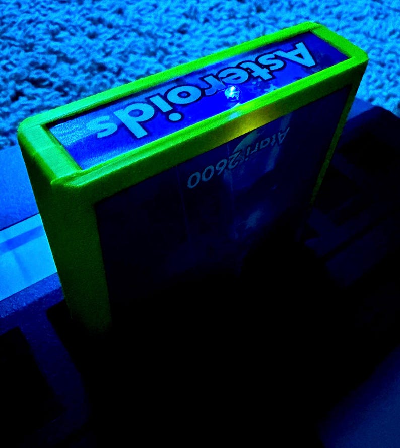 Peut inclure: Une cartouche de jeu vid&eacute;o rectangulaire Atari 2600 pour le jeu Asteroids. La cartouche pr&eacute;sente un bo&icirc;tier en plastique vert citron vif entourant une &eacute;tiquette bleue avec le texte blanc Asteroids et Atari 2600 imprim&eacute; dessus.