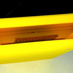 Peut inclure: Une cartouche de jeu vid&eacute;o en plastique jaune vif de forme rectangulaire. Le bord sup&eacute;rieur est ouvert, r&eacute;v&eacute;lant une cavit&eacute; int&eacute;rieure encastr&eacute;e avec deux petites languettes en plastique verticales et un connecteur de carte de circuit imprim&eacute; marron.