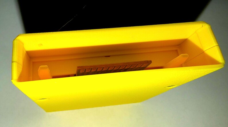 Peut inclure: Une cartouche de jeu vid&eacute;o en plastique jaune vif de forme rectangulaire. Le bord sup&eacute;rieur est ouvert, r&eacute;v&eacute;lant une cavit&eacute; int&eacute;rieure encastr&eacute;e avec deux petites languettes en plastique verticales et un connecteur de carte de circuit imprim&eacute; marron.
