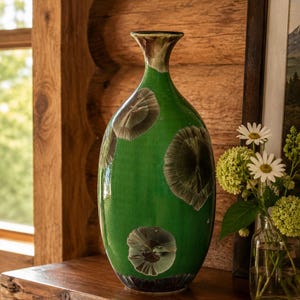 May include: A tall, slender ceramic vase with a glossy, vibrant green glaze featuring distinct, dark, circular crystalline patterns. The vase has a narrow neck that flares slightly at the rim and a rounded body that tapers toward a dark base.