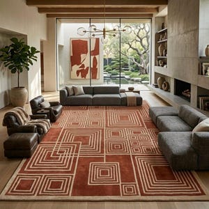 May include: A large rectangular area rug featuring a geometric pattern of concentric squares in shades of terracotta and cream. The rug is positioned in a living room with gray sofas, a leather armchair, a potted plant, and a fireplace.