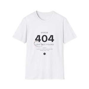 Può includere: Una t-shirt bianca a maniche corte con testo nero che recita ERROR 404 LOVE NOT FOUND. Sotto il testo c'è un cerchio rosso disegnato a mano e il testo aggiuntivo SORRY! CURRENTLY BUSY LOOKING FOR MONEY, NOT LOVE, con una piccola icona circolare.