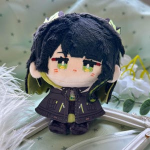 May include: A plush doll with black hair, green eyes, and pale skin. The doll wears a dark gray jacket with lime green accents and a matching collar. The hair features lime green highlights, and the doll has embroidered facial features including red markings under the eyes.