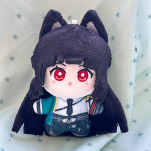 May include: A plush doll featuring a character with dark purple hair, pointed ears, and bright red eyes. The doll wears a white collared shirt with a black tie, a teal jacket, and dark pants. The plush has a soft texture and a small metal loop on top.