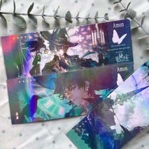 May include: Two rectangular bookmarks featuring holographic anime-style illustrations of a character in a hat with a raven. The text reads Amon, The hands that manipulate the passage of time, and includes Chinese characters. The design has a clock motif.