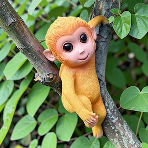 May include: A whimsical, orange-yellow monkey figurine clinging to a tree branch. The monkey has large, expressive eyes and a smiling face. The background features green leaves, creating a naturalistic setting. This decorative item is suitable for garden or home decor.