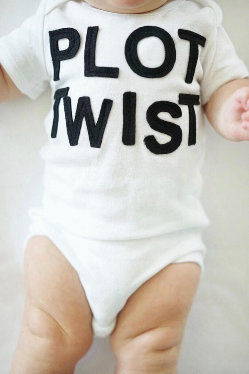 K&ouml;nnte beinhalten: Ein wei&szlig;er Baby-Body mit dem Schriftzug "PLOT TWIST" in gro&szlig;en, schwarzen Blockbuchstaben. Der kurz&auml;rmelige Body bedeckt den Oberk&ouml;rper und die Beine des Babys und bietet ein schlichtes, klares Design.