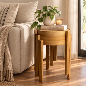 Peut inclure: Une table d'appoint ronde en bois au fini brun clair, dotée d'un plateau cylindrique et de quatre pieds verticaux de longueurs variables. Le dessus de la table supporte un pot en céramique blanche mouchetée avec une plante verte et une bougie.