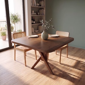 May include: A square dark wood dining table with a cross-leg base, accompanied by two light wood chairs featuring woven cane backrests. A light green ceramic vase with eucalyptus stems sits in the center, flanked by two white plates.
