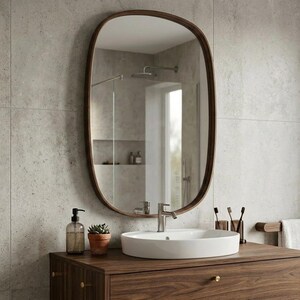 May include: A contemporary bathroom scene featuring a dark wood vanity unit with a white oval basin and a large, oval mirror with a dark wood frame. A small potted plant and soap dispenser are on the countertop. The wall is tiled with light grey tiles.