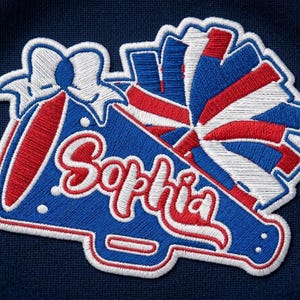May include: An embroidered patch on a dark blue fabric background featuring a blue megaphone with a white bow and a red, white, and blue pom-pom. The name Sophia is stitched in white cursive script with a red outline across the megaphone body.