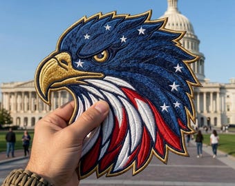 May include: An embroidered patch shaped like an eagle head, featuring a gold beak and eye, with feathers colored in deep blue, white, and red. The blue section is accented with several white embroidered stars, and the entire patch has a gold border.