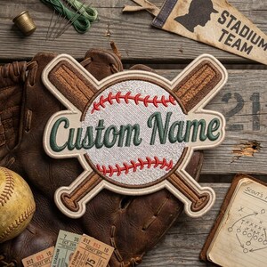 May include: An embroidered patch featuring a white baseball with red stitching crossed by two brown wooden baseball bats. The patch displays the text Custom Name in dark green cursive script. The design is outlined in a light tan border.