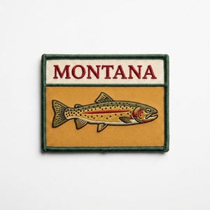 May include: A rectangular embroidered patch featuring the word MONTANA in red capital letters on a cream background above a golden yellow section displaying a detailed trout fish with olive green, brown, and red accents, all bordered by dark green.