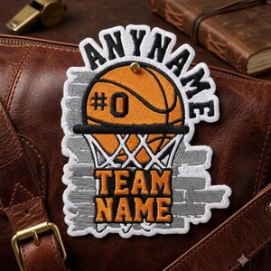 May include: An embroidered patch featuring an orange basketball with the number 0, a white net, and grey brick-patterned background. The patch includes the text ANYNAME at the top and TEAM NAME at the bottom in bold black and orange lettering.