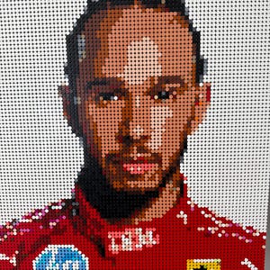 May include: A portrait created from small, coloured dots, depicting a person in a red racing suit with logos and a yellow and black emblem. The background is white, and the artwork is mounted on a wooden easel.
