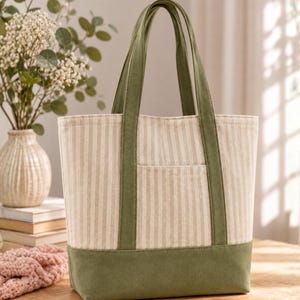 Peut inclure: Un sac cabas doté d'un motif à rayures verticales beiges et blanches sur le corps principal, complété par une base en tissu vert olive uni et deux anses assorties de la même couleur. Le sac comprend une petite poche extérieure sur le devant.