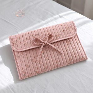 May include: A pink quilted fabric case with a floral pattern and a bow closure. The case has a flap and is lying on a white surface. The text "STEP BY STEP GUIDE BEGINNER FRIENDLY" is printed at the bottom.
