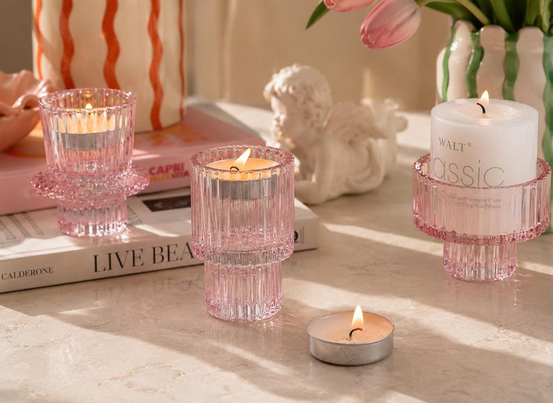 Pink glass tealight candle holders styled on a neutral stone tabletop with books, tulips, and soft editorial lighting.