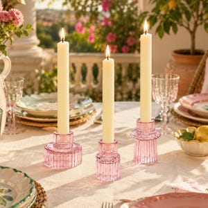 Pink double head candle holders with white taper candles on a sunlit outdoor terrace tablescape with floral tableware and soft greenery.