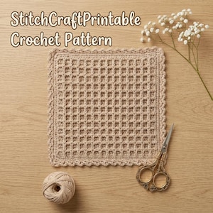 Op de afbeelding: Een vierkant beige haakwerk met een wafelsteekpatroon en een geschulpte rand. De tekst StitchCraftPrintable Crochet Pattern is zichtbaar. Een bol beige garen en een metalen schaar liggen naast het haakwerk.