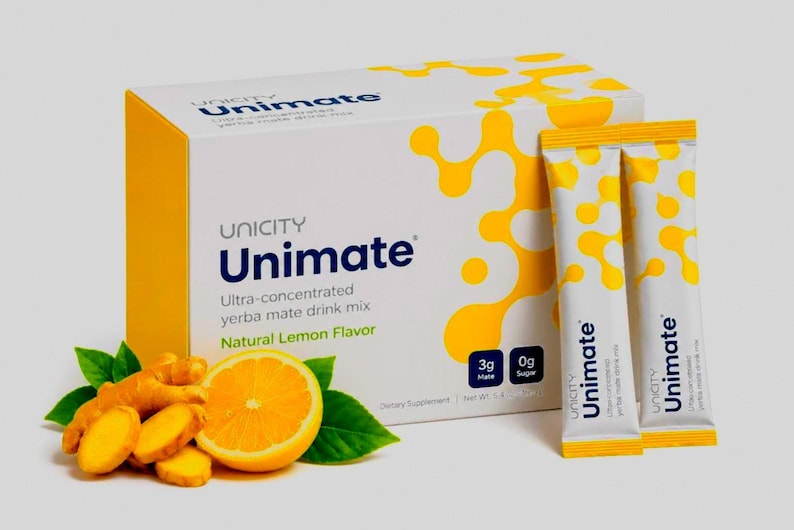 May include: A white and yellow box of Unicity Unimate ultra-concentrated yerba mate drink mix with natural lemon flavor, accompanied by two matching single-serve packets, fresh ginger root, and a sliced lemon with green leaves on the side.