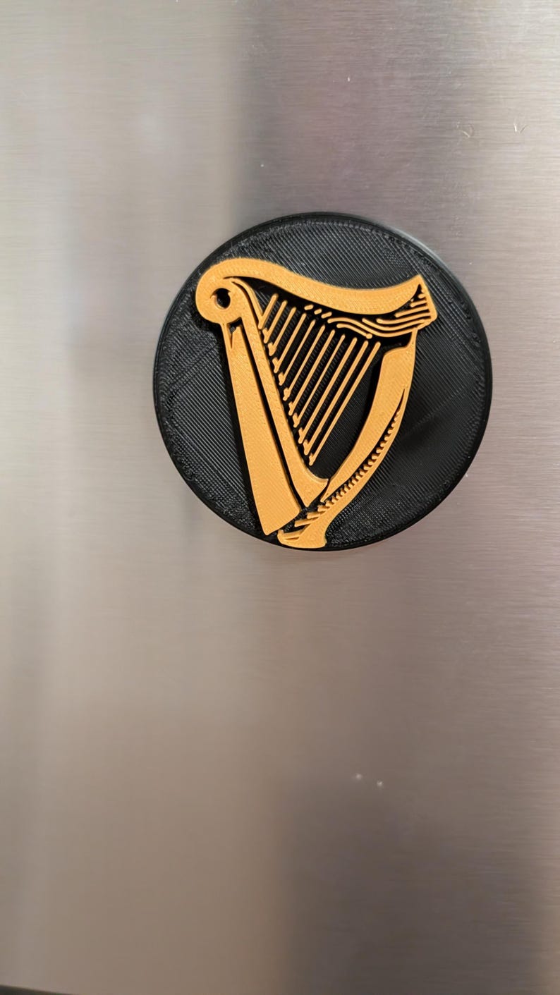 May include: A round, black and gold emblem featuring a harp design. The harp is gold and set against a black background. The emblem is likely a logo or a decorative item.