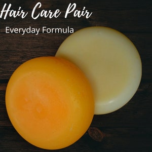 May include: Two round hair care bars, one yellow and one light beige, on a dark wood surface. The text "Hair Care Pair Everyday Formula" is above the bars.