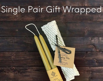 May include: A pair of olive green taper candles connected by a white wick, wrapped in a tan paper band labelled Scenter Square Authentic Bayberry Wax. A second pair is encased in white protective honeycomb paper with a tied tag reading Bayberry Wax.