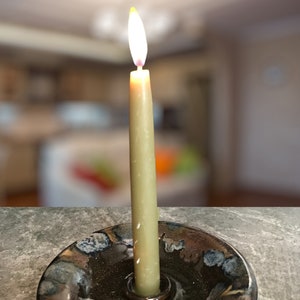 May include: A lit candle in a black ceramic candle holder with a blue and brown glaze. The candle is a light brown colour and is burning brightly.