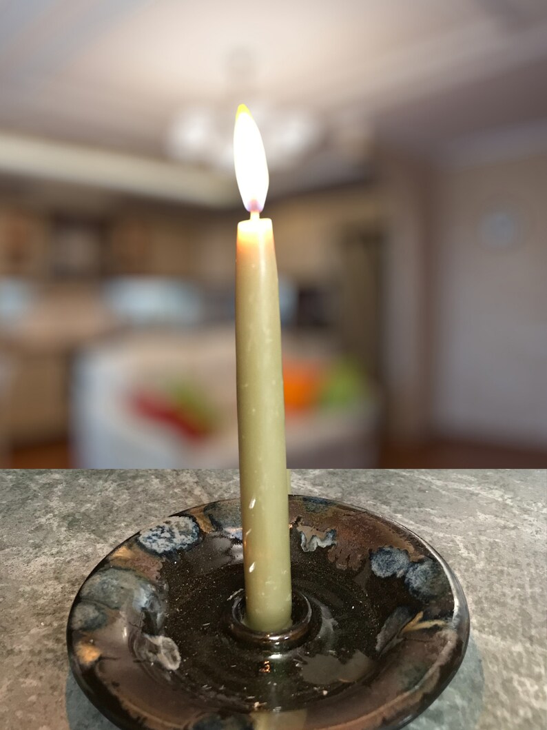 May include: A lit candle in a black ceramic candle holder with a blue and brown glaze. The candle is a light brown colour and is burning brightly.