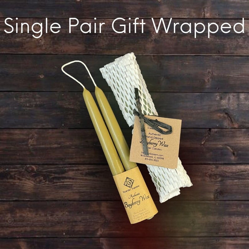 May include: A pair of yellow beeswax candles wrapped in a white and green mesh gift bag. The candles are labeled "Authentic Hand Dipped Bayberry Wax Candles" and "Scents of Square.com, Woodstock, IL 60098, 815-814-1000".