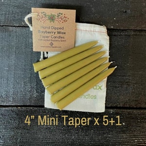 May include: A set of six 4-inch mini taper candles in a natural beige colour, packaged in a white muslin bag with a brown paper tag that reads "Hand Dipped Bayberry Wax Taper Candles With Added Bayberry Scent" and a website address. The bag also has the words "Wax" and "Candles" printed on it. The text "4" Mini Taper x 5+1" is printed below the image.