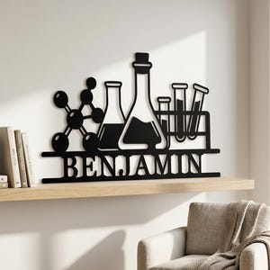 Peut inclure: Une décoration murale en métal noir représentant une structure moléculaire, un grand erlenmeyer et deux tubes à essai dans un support, avec le nom BENJAMIN découpé en lettres capitales sur la barre horizontale inférieure du motif.