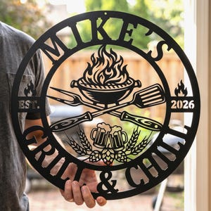 May include: A circular black metal wall sign featuring the text MIKE'S GRILL & CHILL, EST. 2026. The design includes a central flaming grill, crossed barbecue utensils, two beer mugs, and wheat stalks, all cut from a single piece of metal.