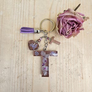 Könnte beinhalten: Ein Schlüsselanhänger mit einem Buchstaben-T-Anhänger aus braunem Harz mit eingebetteten violetten Blumenelementen, einem kleinen braunen Herzanhänger mit violetten Herzakzenten, einer violetten Quaste, einem Buchstaben-T-Anhänger und einem silberfarbenen Metallring.