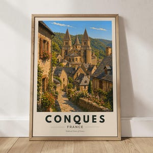 May include: A framed travel poster featuring a stone village in Conques, France, with a large cathedral, cobblestone path, and flowers. The text reads CONQUES FRANCE Medieval Heart of France in dark green letters on a cream background.