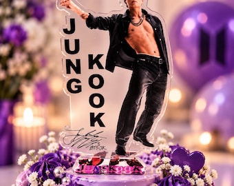 May include: A clear acrylic cake topper featuring a printed image of Jungkook from BTS, wearing an unbuttoned black shirt and black jeans. The text JUNG KOOK and a signature are printed on the acrylic. The base displays the name JUNGKOOK.