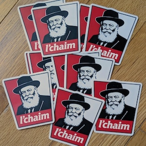 Peut inclure: Une collection d'autocollants rectangulaires présentant une illustration graphique d'un homme barbu portant un chapeau et un costume noirs. Le design comprend un fond rouge et le texte blanc l'chaim imprimé au bas de chaque autocollant.
