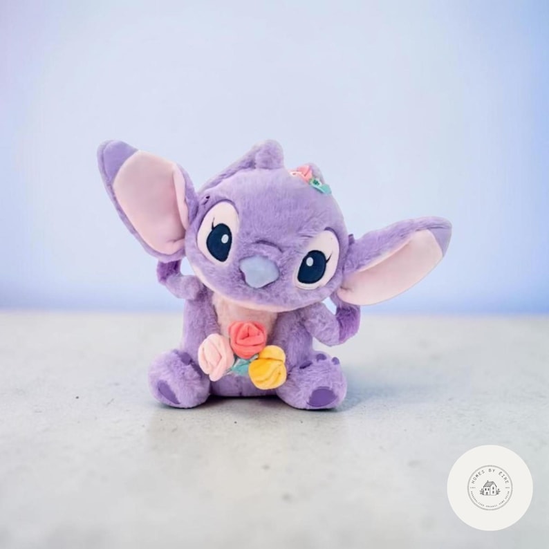 May include: A plush, lavender-colored character with large ears and big eyes, adorned with a floral arrangement. The stuffed animal has a light blue nose and pink inner ears. The toy is a popular character from a well-known animated film.